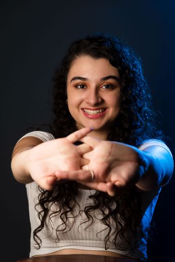 Close-up portrait of young beautiful woman with hands forward, smiling. Looking at the camera. Against gray background.