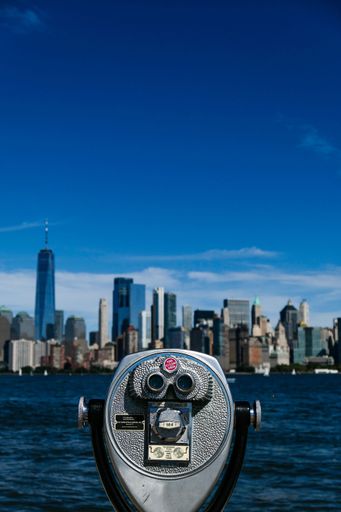 A vertical shot of binoculars with the New York skyline and Hudson river in the background.