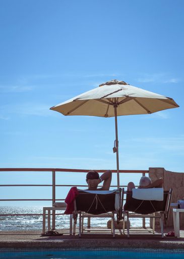 A vertical shot of people on lounge chairs under a beach umbrella on a seashore