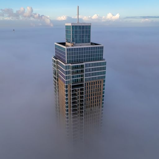 A high-rise skyscraper stands tall above the wispy clouds in Rotterdam, Netherlands