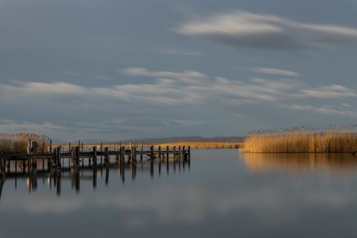 A wooden pier near the sea reflecting on it under the beautiful cloudy sky