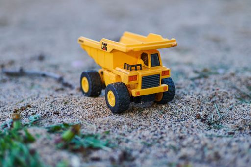 A small toy truck on the ground in a natural outdoor environment, surrounded by dirt