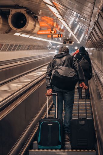 A male with travel bags on an escalator exiting underground subway platform