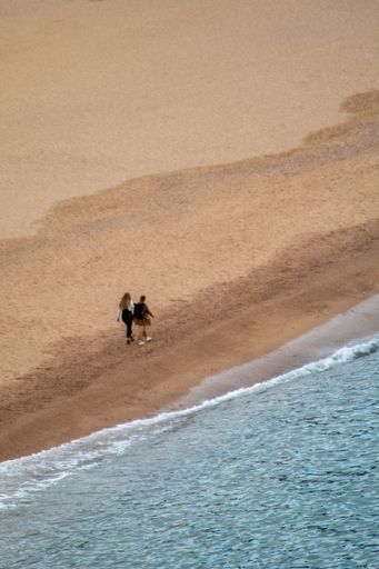 Two people walking near shallow waters in the beach coastline, enjoying the beautiful day