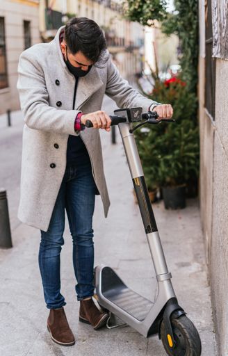 A vertical shot of a stylish guy with his hands on an electric scooter wearing a face mask - concept of the new normal