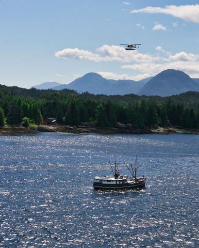 A Seaplane flying over a fishing boat on a sunny day in Alaska