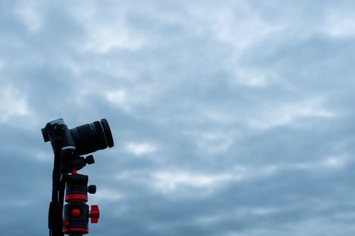 A selective focus shot of a camera on a tripod under the cloudy sky