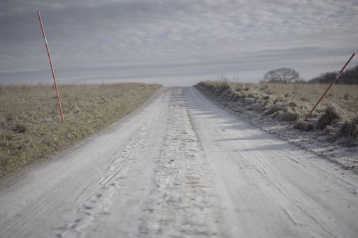 A scenic view of a sand path going through an open field seen on a cloudy day