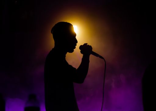 A silhouette shot of a man singing using a microphone inside a club with purple smoke around him