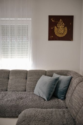 A gray couch in a room with a painting with Islamic calligraphy hanging on the wall
