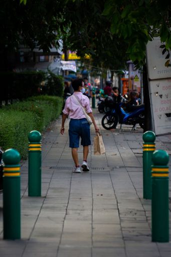 A vertical shot of a man with a paper bag walking down the street. Bangkok, Thailand.