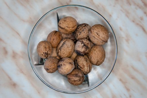 The white bowl with black edges on the table, filled with some walnuts