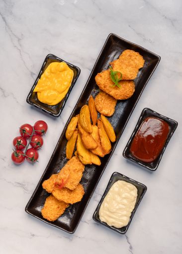 A top view of a platter of fried meat and potatoes near bowls of condiments