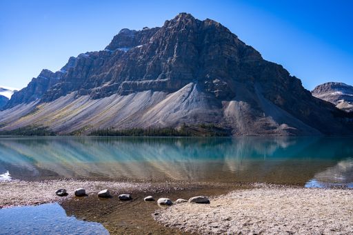A magnificent view of a transparent mountain lake's surface, with an evergreen forest and a rocky mountain in the background, on a sunny day