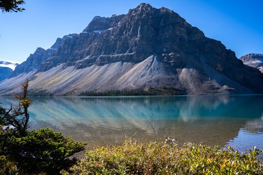 A magnificent view of a transparent mountain lake's surface, with an evergreen forest and a rocky mountain in the background, on a sunny day