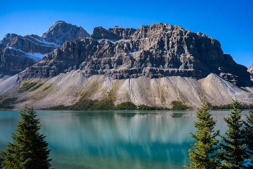 A magnificent view of a transparent mountain lake's surface, with an evergreen forest and a rocky mountain in the background, on a sunny day