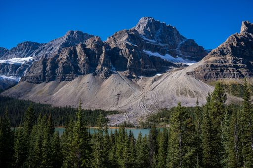 A magnificent view of a glacier mountain lake, surrounded by evergreen forest, with snowy slopes and mountain tops in the background, on a sunny day