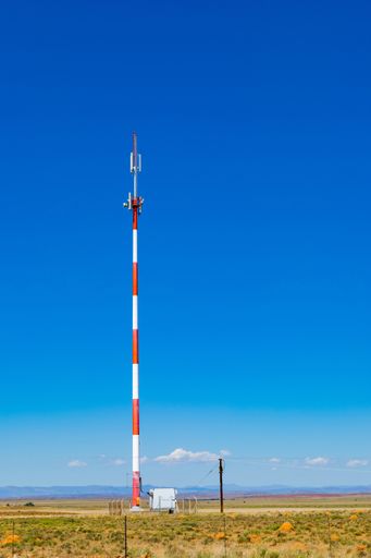 A vertical shot of a striped cell phone tower in the countryside of South Africa under a blue sky