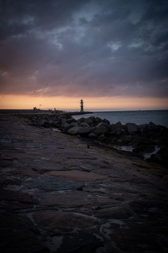 A vertical shot of a lighthouse is visible as the sun sets on the horizon