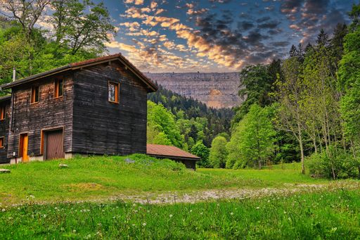 A picturesque view of a mountain landscape featuring a cozy wooden cabin in the foreground with a lush forest on the other side.