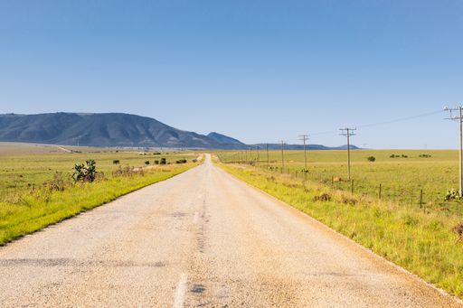 A straight rural road going through a grassy plain landscape in South Africa under a clear blue sky