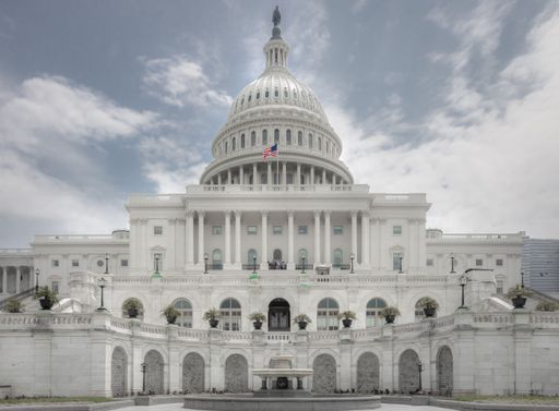 A horizontal picture of the US Capitol with the flag in Washington, DC, against a blue cloudy sky