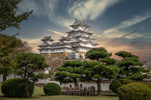 A breathtaking low-angle shot of a hilltop Japanese castle complex in the city of Himeji, Japan, surrounded by green trees on a sunny day
