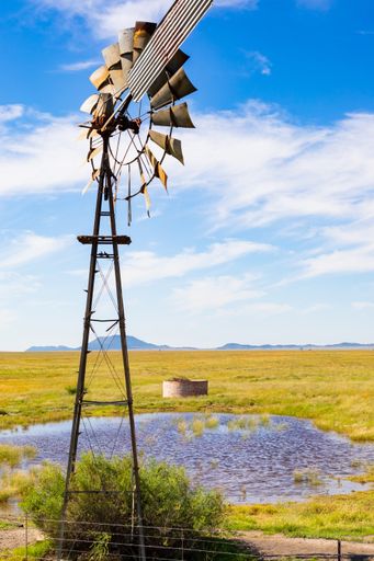 A vertical shot of an old vintage windmill near a small pond under a beautiful cloudscape in South Africa