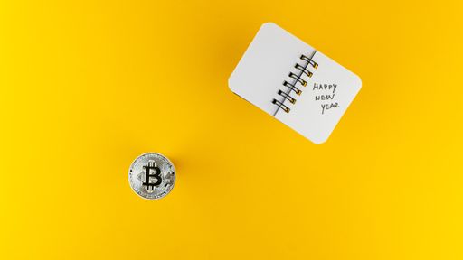 An overhead shot of a Bitcoin and a small notebook with Happy New Year text on it