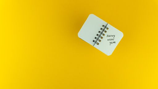 An overhead shot of a small notebook with Happy New Year text on it on a yellow background