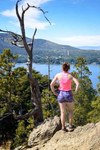 A young Caucasian female standing on mountain peak backward with a beautiful lake in the background