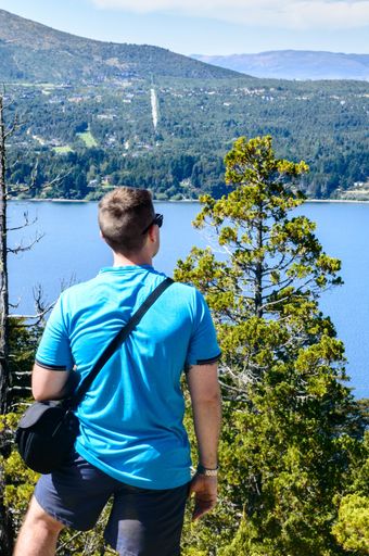 A young Caucasian male admiring the beautiful view of a lake from the mountain peak