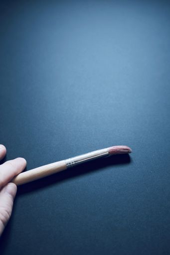 A vertical high angle shot of a hand holding a painting brush on blue surface