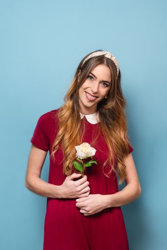 A young happy woman in a red dress smiling and holding a white flower as Valentine's present against a blue background