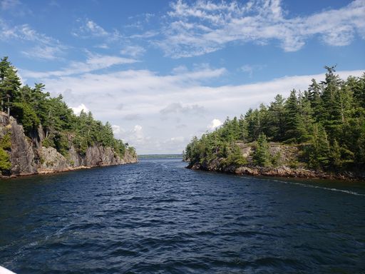 A scenic shot of a narrow waterway surrounded by two lands with green trees on them on a sunny day