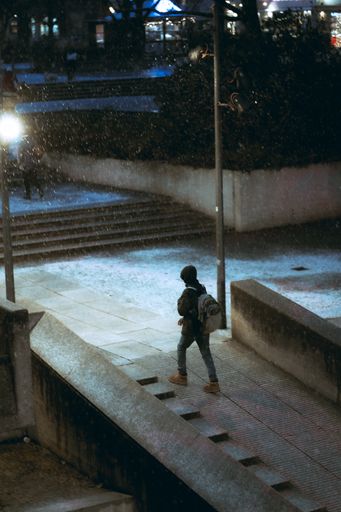 A young stylish man in a winter jacket walking on the street under the snow at night