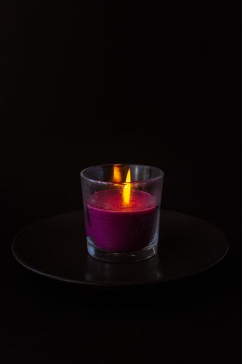 A vertical shot of a purple lit glass candle isolated on black backgroun