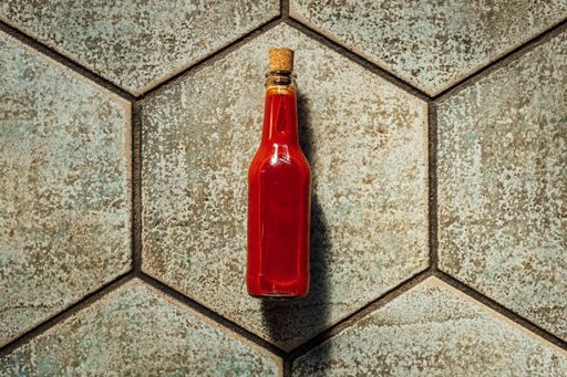 A closeup of a bottle of hot sauce in the cobblestone surface