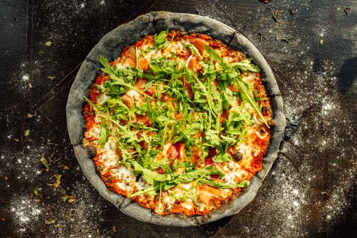 A closeup of a plate of pizza with Arugula on the black table