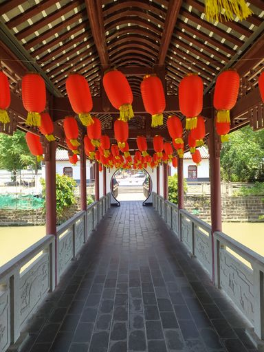 A vertical shot of red Asian lanterns hanging from the wooden roof above a fenced walkway