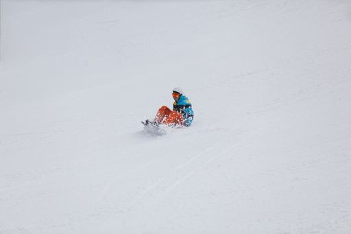 A snowboarder in colorful clothing falling on the slope during freestyle ski competition.