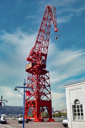 A vertical shot of a red container crane next to the Bilbao Maritime Museum