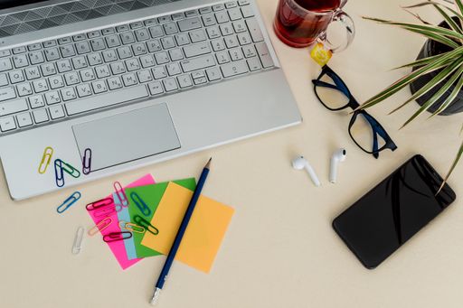 A top view of a laptop on the table with colorful notes, paper clips, and headphones with a phone on it