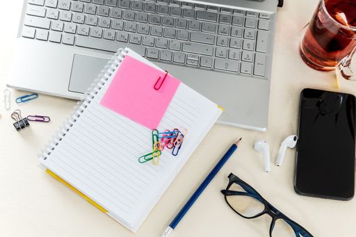 A top view of colorful paper clips on a blank notepad on a laptop with headphones and a phone on the table