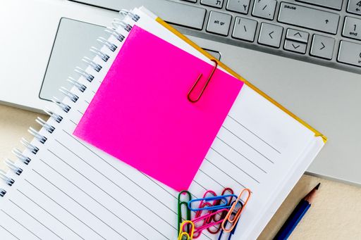 A top view of colorful paper clips on a blank notepad on a laptop