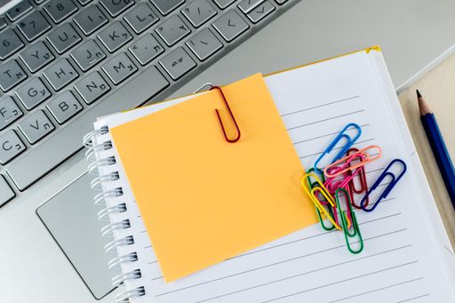 A top view of colorful paper clips on a blank notepad on a laptop