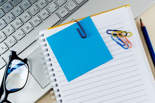 A top view of colorful paper clips on a blank notepad on a laptop