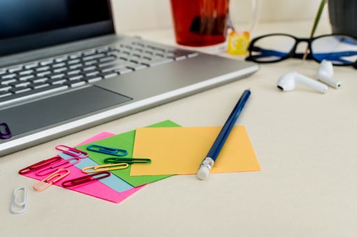 A closeup of colorful notes with paper clips, headphones, laptop, and a pencil on the table