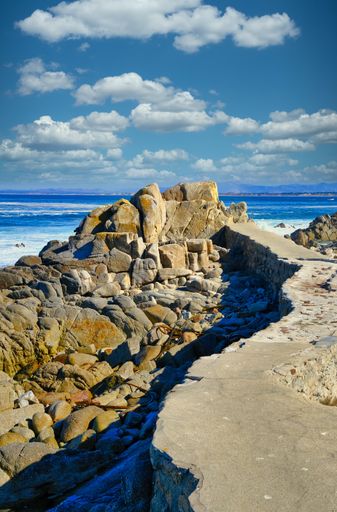 A vertical shot of a lot of rock formations on the beach under the beautiful cloudy sky
