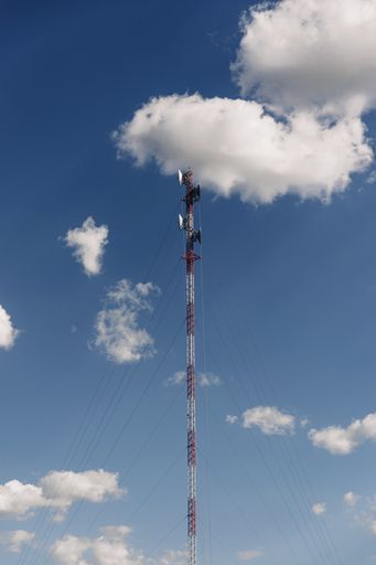 A vertical shot of a mast tower against the blue cloudy sky